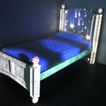 A white bedframe with purple bed, lights being projected onto the headboard