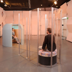 Two people sitting inside enclosures that are part of an interactive art installation (650x470)