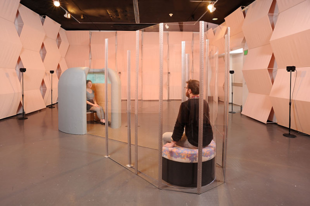 Two people sitting inside enclosures that are part of an interactive art installation (650x470)