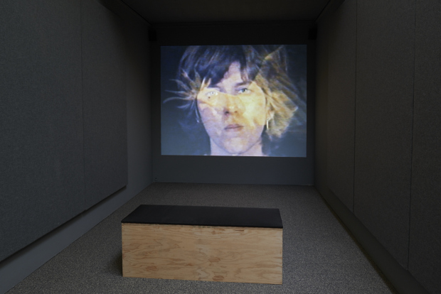 A black room, a chair, and a movie of a man being projected on the wall