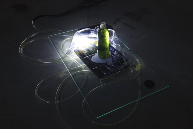 A glass platform, cable with light, a device, and a bottle of yellow liquid (cropped)